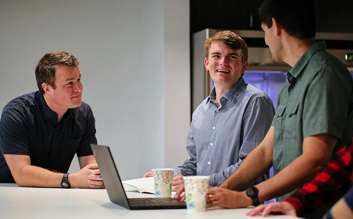 Three OuterBox WooCommerce SEO Agency team members reviewing campaign strategy on a laptop in a meeting room