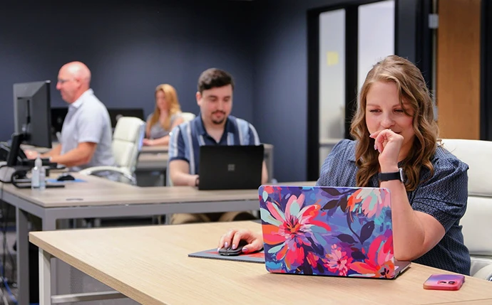 OuterBox WordPress SEO team working at desks in an open office, with a strategist on a floral-patterned laptop