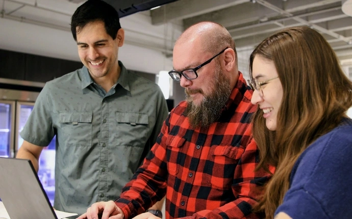 Three OuterBox SEO link builders collaborating around a laptop in the agency office
