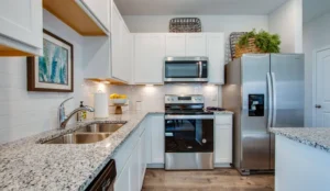 A bright D.R. Horton model-home kitchen with white shaker cabinets, granite countertops, and stainless steel appliances