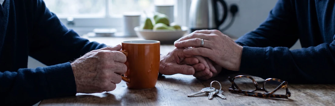 Adult child and parent discussing senior living options together at a kitchen table, with house keys and reading glasses beside them