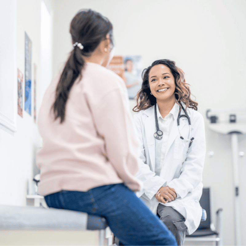 Clinician in a white coat talking with a patient in an exam room